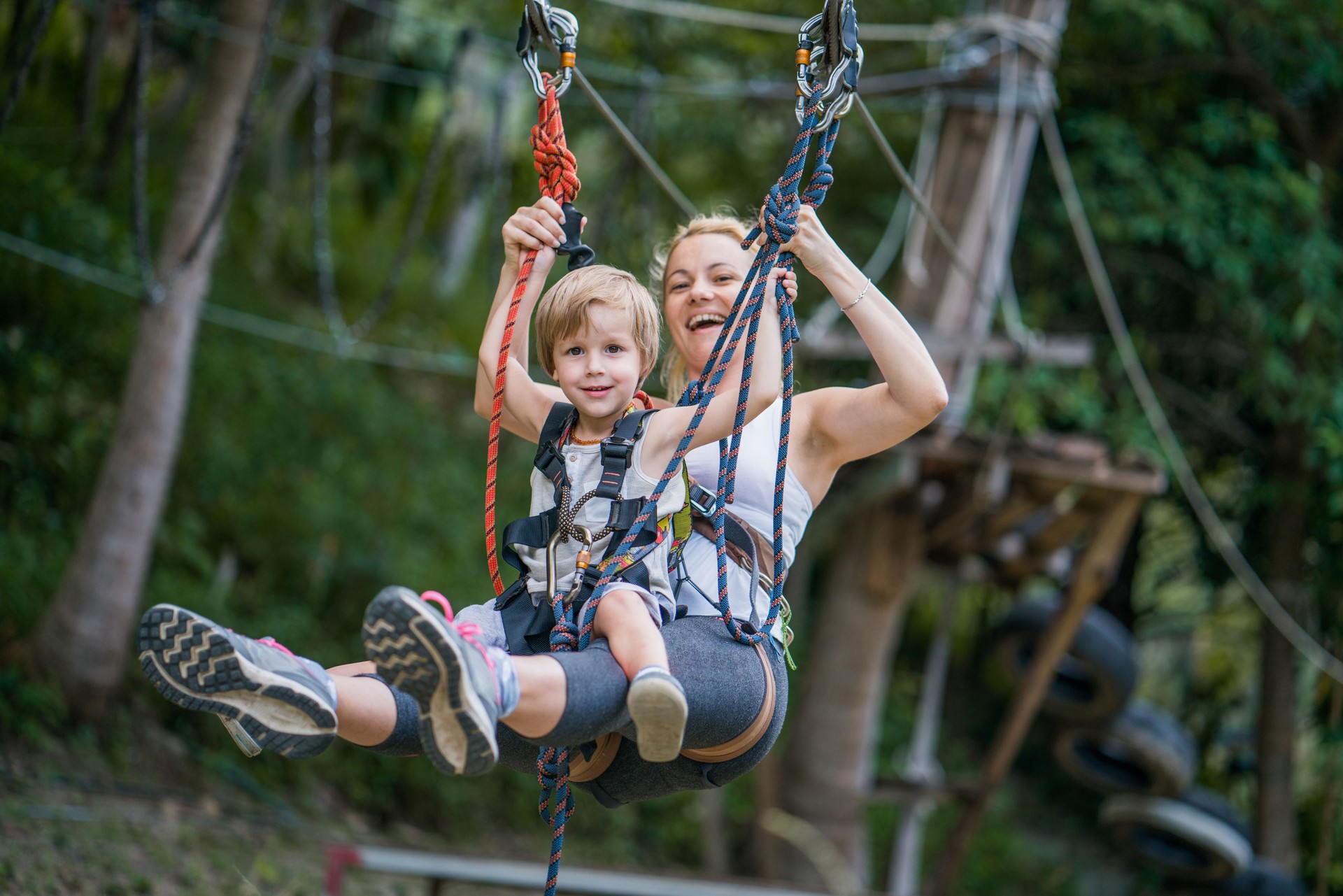 Happy mother and son having fun while zip lining in the forest.