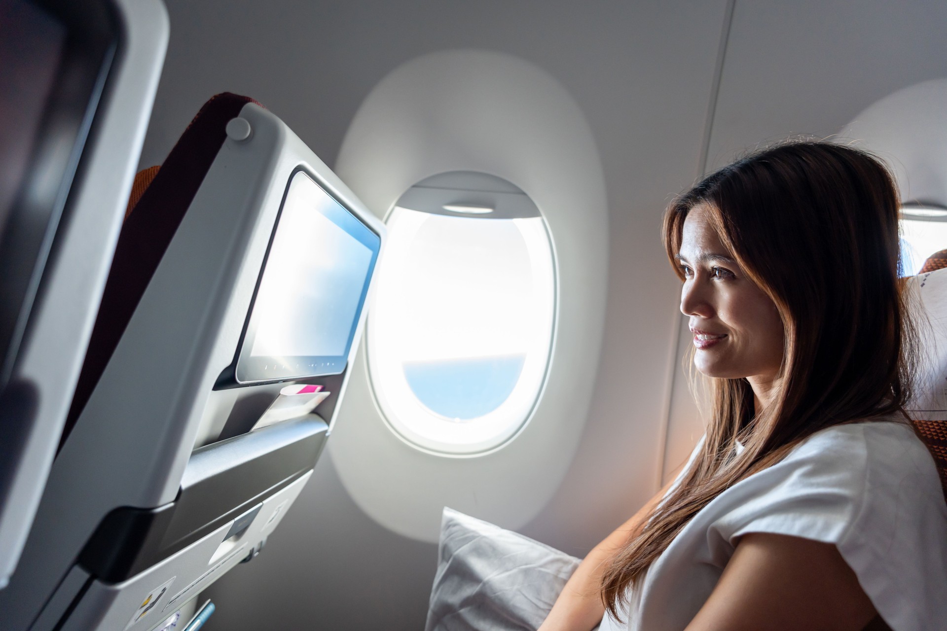 Asian woman watch a movie during a long international flight in airplane. Attractive female traveler sitting on window seat, spend time travel during holiday vacation trip by aeroplane transportation.